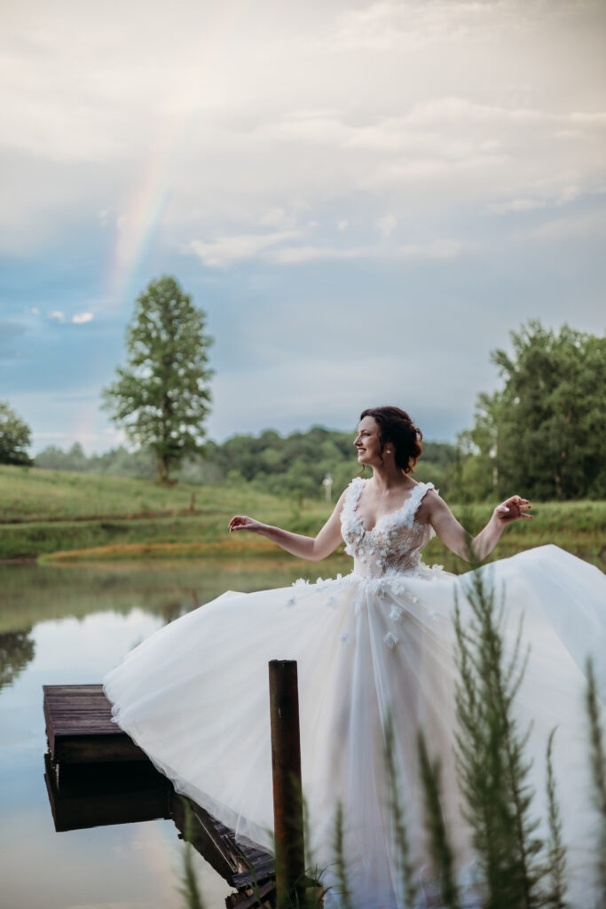  A bride stands in front of a rainbow after a rainy outdoor wedding.