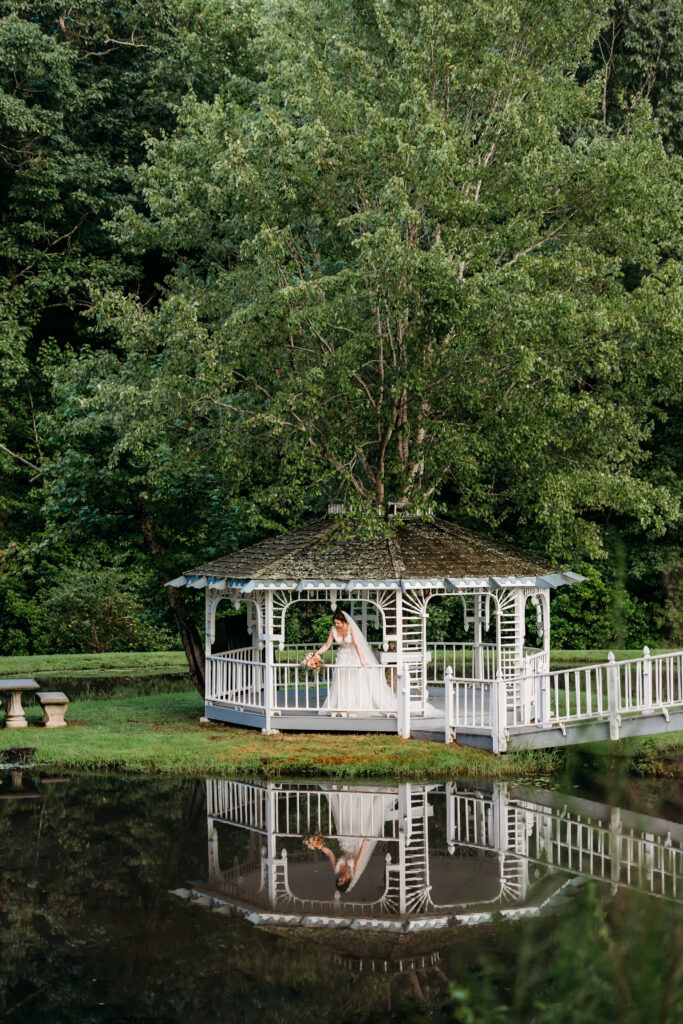 A bride poses in the gazebo after a rain storm enjoying her reflection in the water