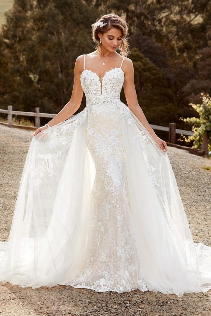 A bride wears a fitted gown with a lace over skirt 2025 trending wedding gown style