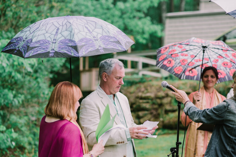 Wedding guests stand under umbrellas on a rainy Saturday outdoor wedding in Greenville South Carolina