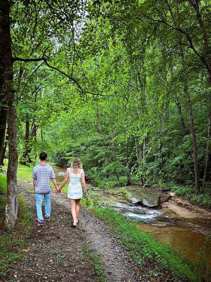 A couple walks along the river looking for a spot for their outdoor elopement ceremony at a wedding venue near Greenville South Carolina