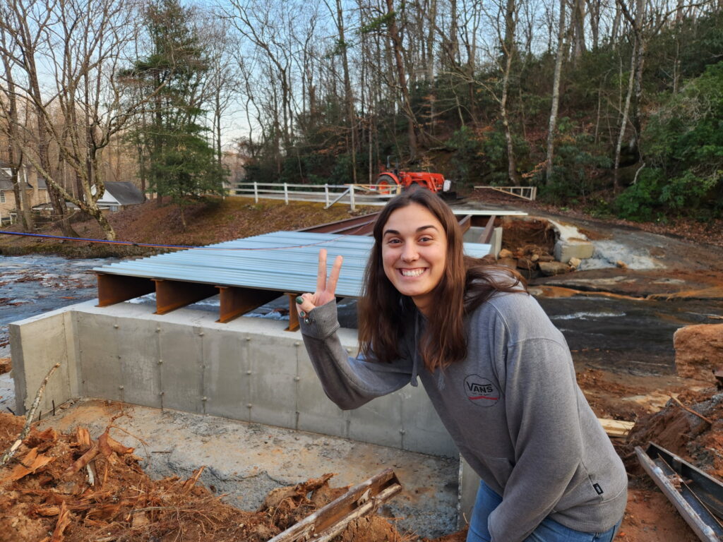 Abby Zordan gives the victory sign in front of bridge construction across the middle Tiger River at a wedding venue in Landrum South Carolina. The concrete pans are partially set in the background