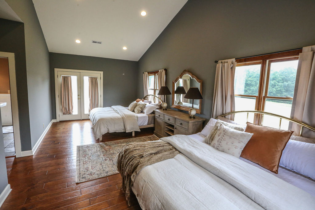 Luxuriously appointed double king bedroom with blue gray walls, white linens, antique furniture, and French doors to outside