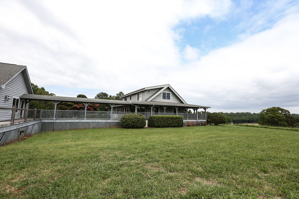  A gray farmhouse with a 360° wraparound porch and an outbuilding attached by a portico with beautiful meadow views