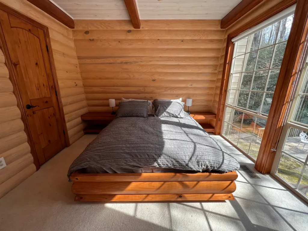 Floor to ceiling windows let in plenty of natural light to this second bedroom in this cozy log cabin