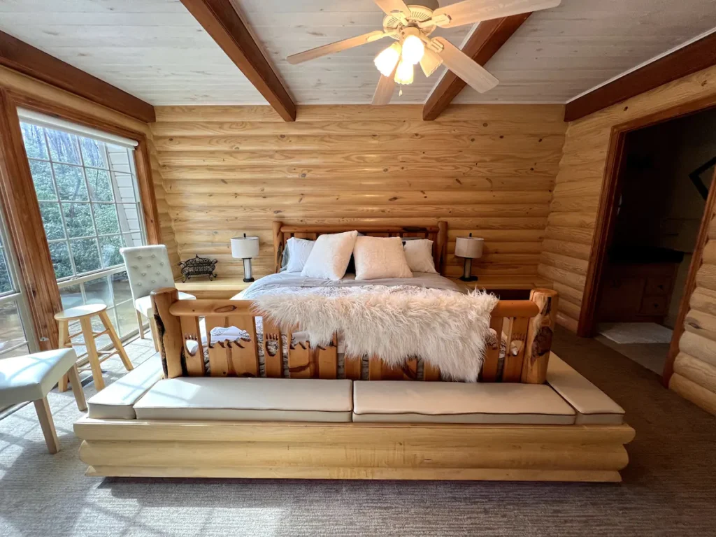 King size bed with wraparound benches and floor ceiling windows in the primary bedroom in this cozy log cabin
