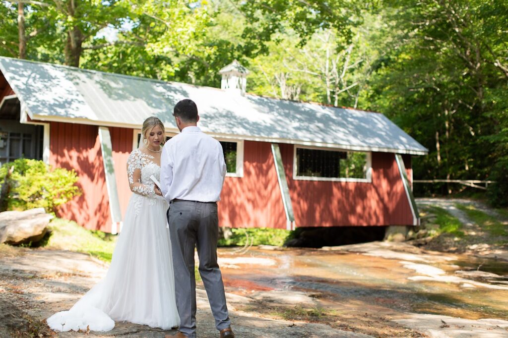 Bride, Groom and wedding party pose for wedding days photos by a covered bridge at their garden wedding venue near Greenville SC