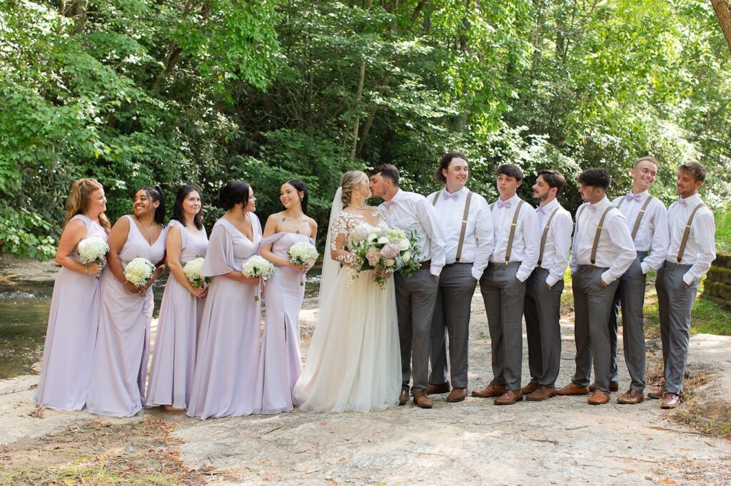 A spring wedding in Greenville SC, the bridesmaids are wearing lilac pink bridesmaid dresses, the groomsmen in a grey suit, the bride is holding an elegant bouquet of fresh flowers of soft pink, creme & green.